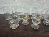 bottles and glasses are lined up on a table with a pitcher in the background