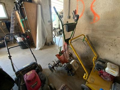 Plusieurs tondeuses à gazon sont alignées contre un mur dans un garage