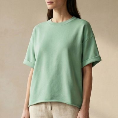 une femme debout devant un mur beige, vêtue d'un haut vert