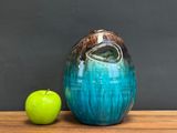 a green apple next to a blue vase on a wooden table