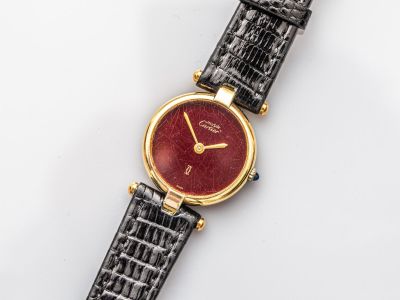 un gros plan d'une montre posée sur une surface blanche, avec un cadran rouge