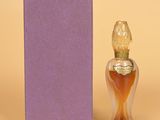 un flacon de parfum posé à côté d'une boîte violette sur une surface beige