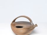 une image représentant un petit vase marron muni d'une anse, posé sur une surface blanche