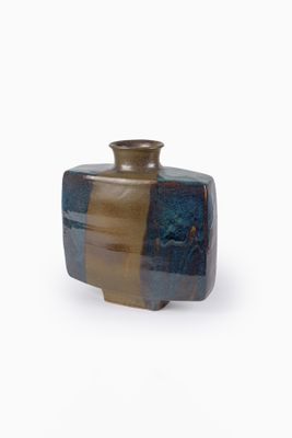 un vase brun et bleu posé sur une surface blanche