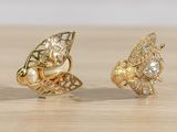 pair of gold tone earrings with pearls and a bee on a wooden surface