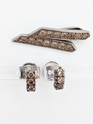 two pieces of silver and diamond jewelry on a white surface
