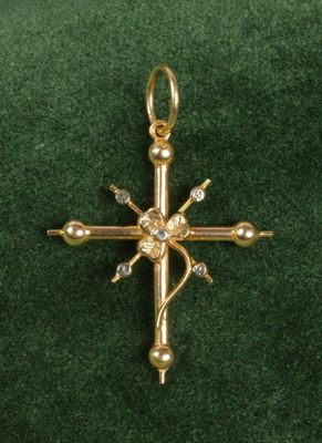 pendentif en forme de croix plaqué or, orné de pierres en cristal transparent, sur un fond de velours vert