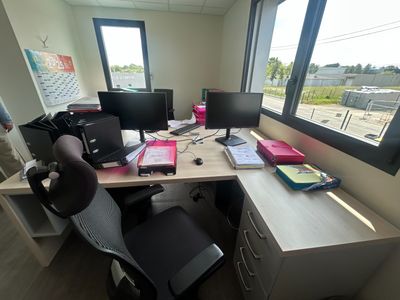 un bureau équipé de deux écrans d'ordinateur et d'une chaise, placé devant une fenêtre