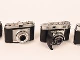 four old cameras are lined up in a row on a white surface