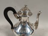 une théière ancienne en argent avec une poignée noire sur une surface blanche