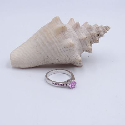 Une image représentant une bague sertie d'un saphir rose côtoie un coquillage