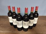 six bottles of red wine are lined up on a wooden table