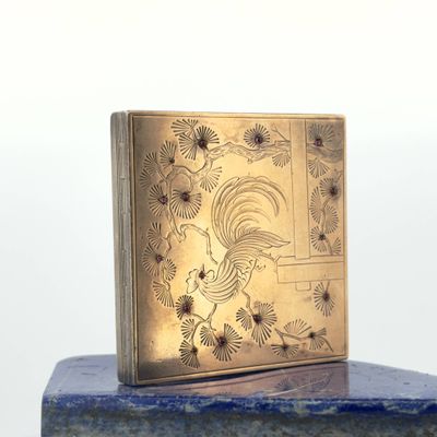 a gold box with a rooster on it sitting on a marble block