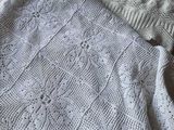 un pull blanc en maille posé sur un lit, à côté d'un oreiller