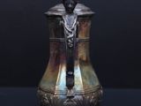 silver vase with a statue on top of it on a black surface