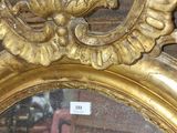 un miroir avec un cadre doré et une chaise rouge en arrière-plan