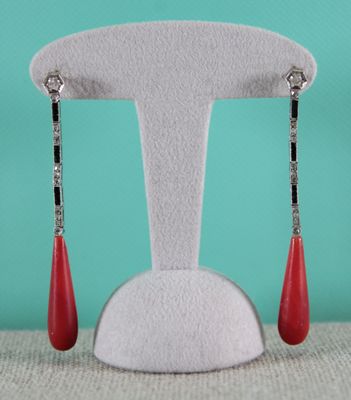 pair of red drop earrings on a white stand against a turquoise background