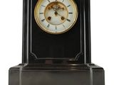 une horloge noire et dorée posée sur un socle, sur fond blanc