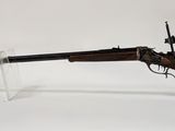 un vieux fusil au canon en bois, posé sur un socle en acrylique transparent
