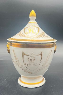a close up of a white and gold covered bowl with a crest on it