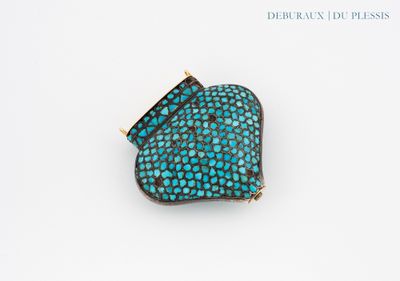 a close up of a turquoise and gold broochle on a white surface