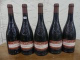 six bouteilles de vin sont posées sur une table devant un mur blanc