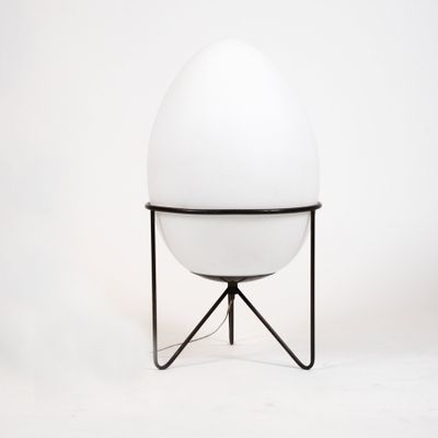 a white egg sitting on top of a metal stand next to a white wall