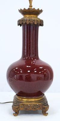 un vase rouge avec un couvercle doré posé sur une table blanche