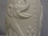 a white vase with a bird on it sitting on a table