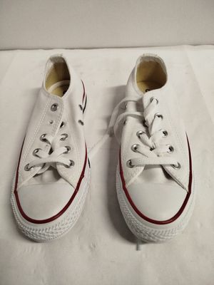 Des Converse blanches aux lacets rouges sont posées sur une surface blanche