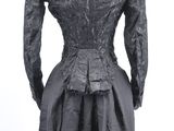 the back view of a black dress with long sleeves and a pleaed skirt