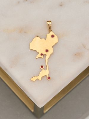 gold plated pendant with a map and ruby stones on a marble surface