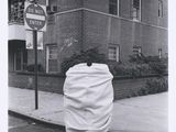 black and white photograph of a person wrapped in a blanket on a street corner