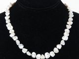 a white pearl necklace on a black mannequin neck