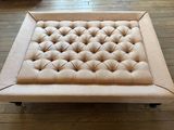 pouf rembourré beige monté sur roulettes, posé sur le parquet du salon