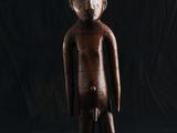 une statue en bois représentant un homme debout sur un fond noir