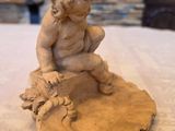 a clay sculpture of a boy sitting on a rock