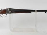 un fusil posé sur un socle transparent, devant un fond blanc