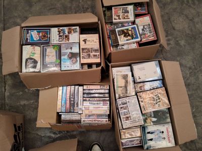 Plusieurs boîtes de DVD sont empilées les unes sur les autres par terre.