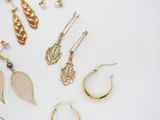 several pairs of gold earrings and rings on a white surface
