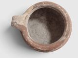 a small clay cup with a handle on a white surface