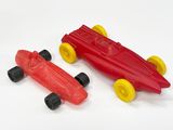 une petite voiture rouge à côté d'une autre petite voiture rouge, posées sur une surface blanche