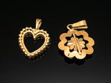 two gold pendants with a heart and a flower on a black surface