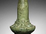 an old green vase sitting on top of a table next to a white wall