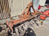 une charrue de tracteur rouillée posée par terre devant un bâtiment