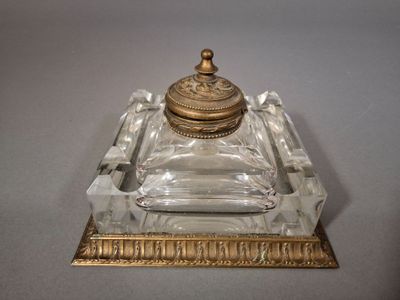 un encrier ancien en verre et laiton, muni d'un couvercle et posé sur un socle