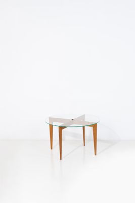 une table avec un plateau en verre et des pieds en bois dans une pièce blanche