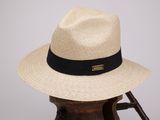 chapeau beige orné d'un ruban noir et d'un autre ruban noir, posé sur un support en bois