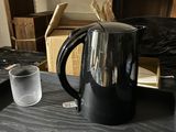 une cafetière noire posée sur un plan de travail, à côté d'un verre d'eau