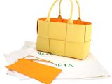 yellow leather handbag with orange handles on a white cloth